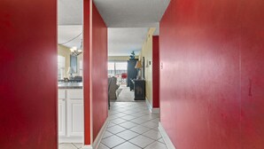 A hallway with red walls and a tiled floor leading to a kitchen area.