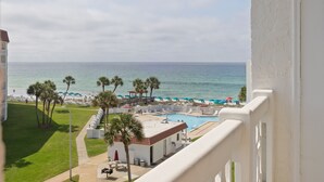 A pool area with a view of the ocean, palm trees, and beach umbrellas.
