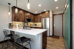 A modern kitchen with a large island, stainless steel appliances, and pendant lighting.