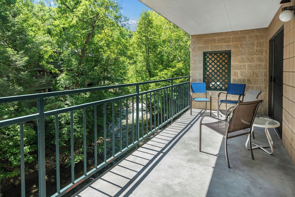 Un balcon donnant sur des arbres, un mur en pierre et un treillage. On y trouve deux chaises et une petite table.