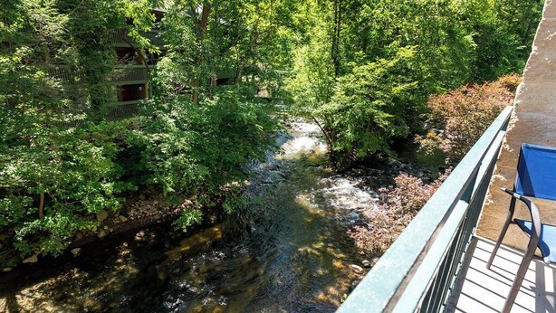 Un río que atraviesa una zona boscosa, con un puente y una silla a la derecha.