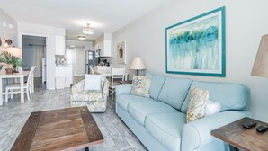 A modern living room with a light blue sofa, a wooden coffee table, and a dining area with white furniture.