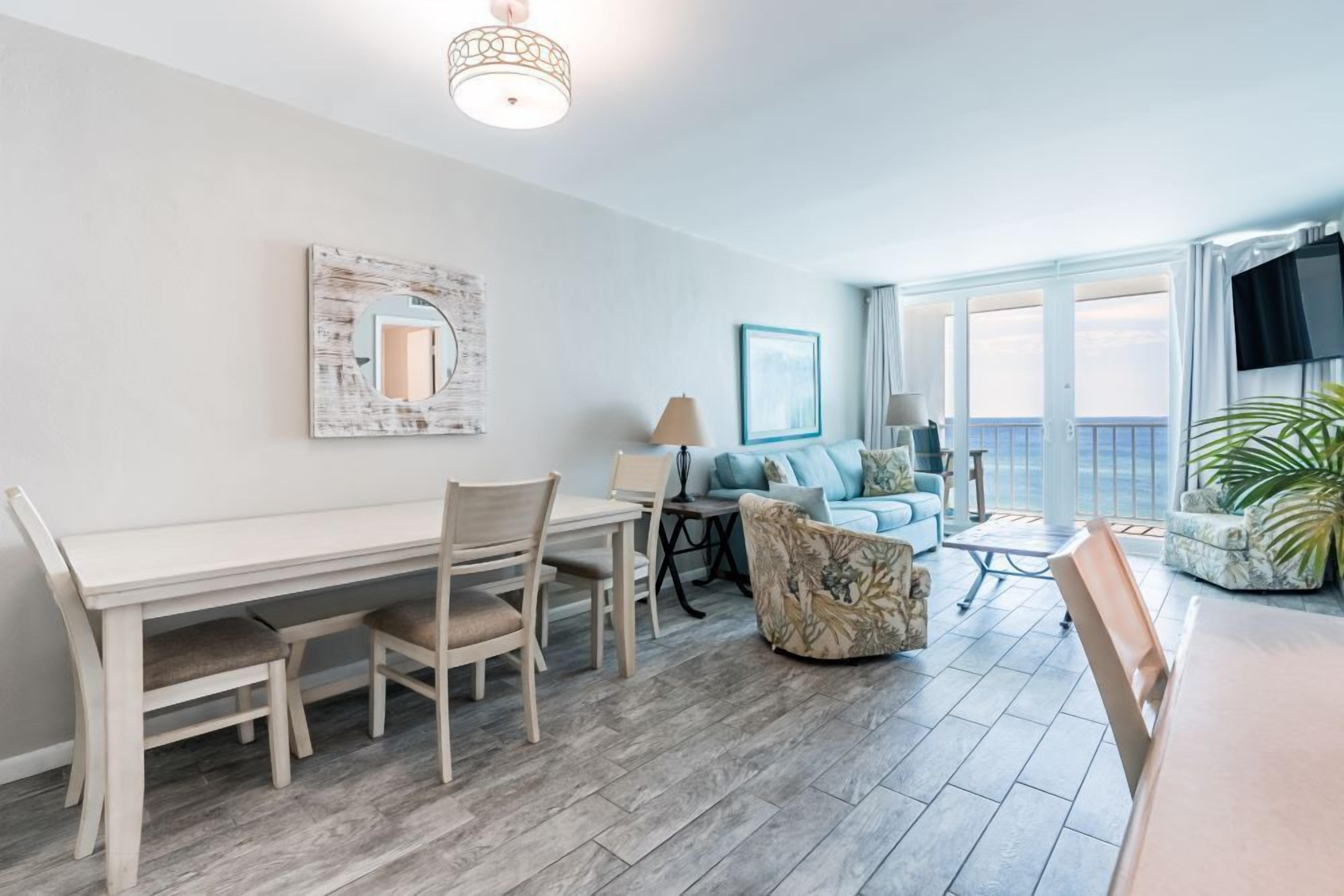 A modern living room with a dining area, a sofa, a TV, and a large window overlooking the sea.