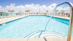 A clear blue pool with a metal ladder, surrounded by white railings and green lounge chairs.