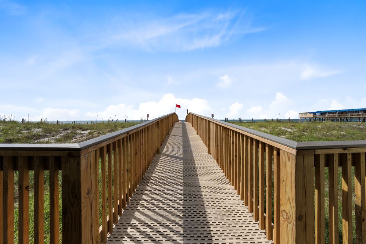 Un muelle de madera que lleva a una zona de playa bajo un cielo despejado.