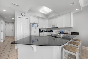 A modern kitchen with white cabinets, a black countertop, and a central island with bar stools.