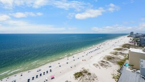 En strand med klart, blått vatten, en sandstrand och byggnader i bakgrunden.