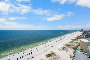 A beach with clear blue water, a sandy shore, and buildings in the background. - Gulf Shores Coastal Beachfront Condo w/ Pool | Sleeps 8 (Gulf Shores)