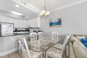 A modern kitchen with white cabinets, a glass dining table, and a chandelier.