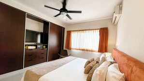 Habitación de hotel con cama, escritorio, silla, ventilador de techo y ventana con cortinas.