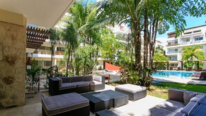 Zona junto a la piscina con mobiliario exterior, palmeras y vistas a una piscina.