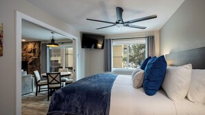Quarto de hotel moderno com uma cama grande, ventilador de teto, TV e vista para o exterior através de uma janela.