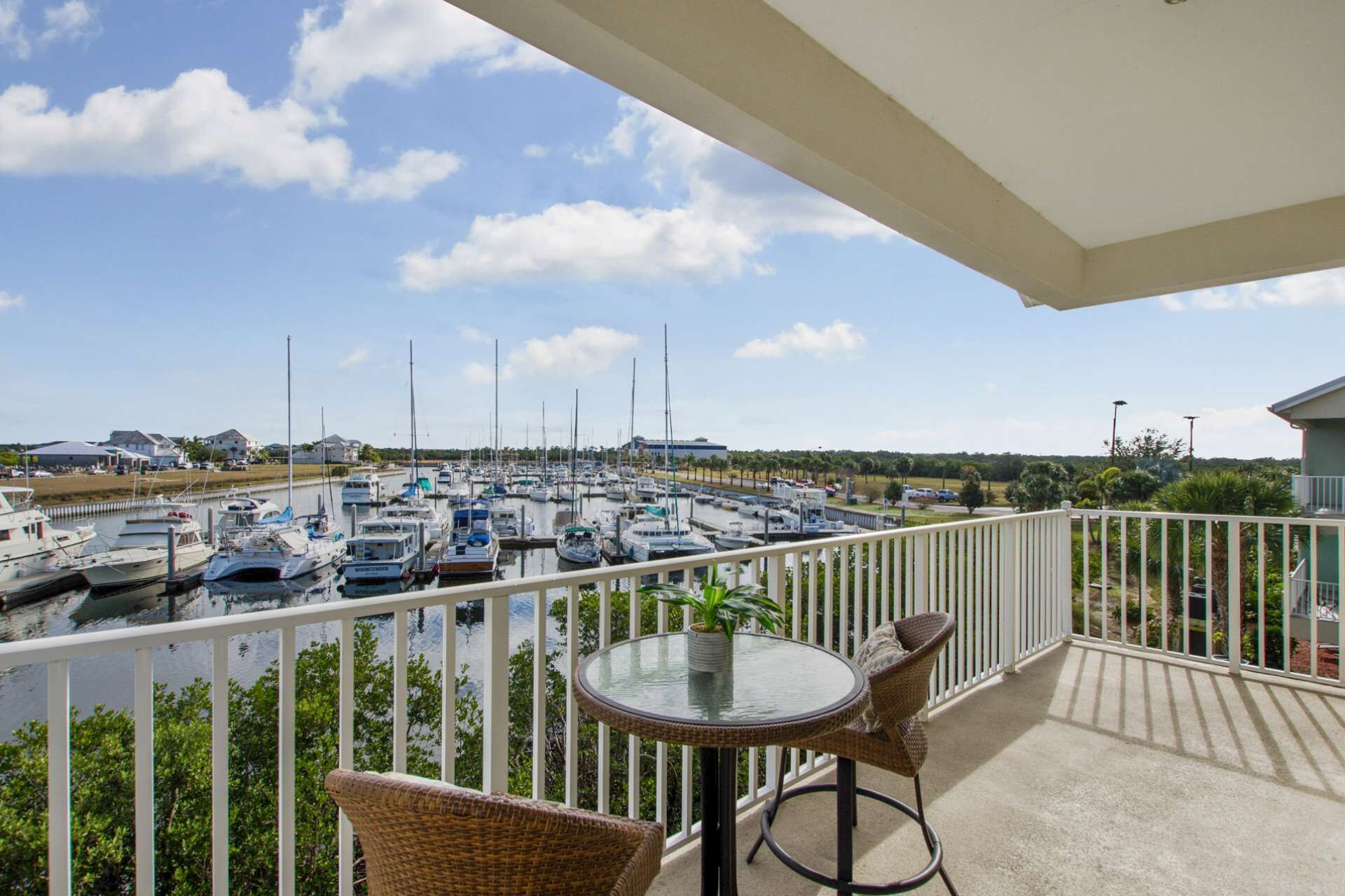 A balcony with a view of a marina filled with boats, a round table, and wicker chairs.