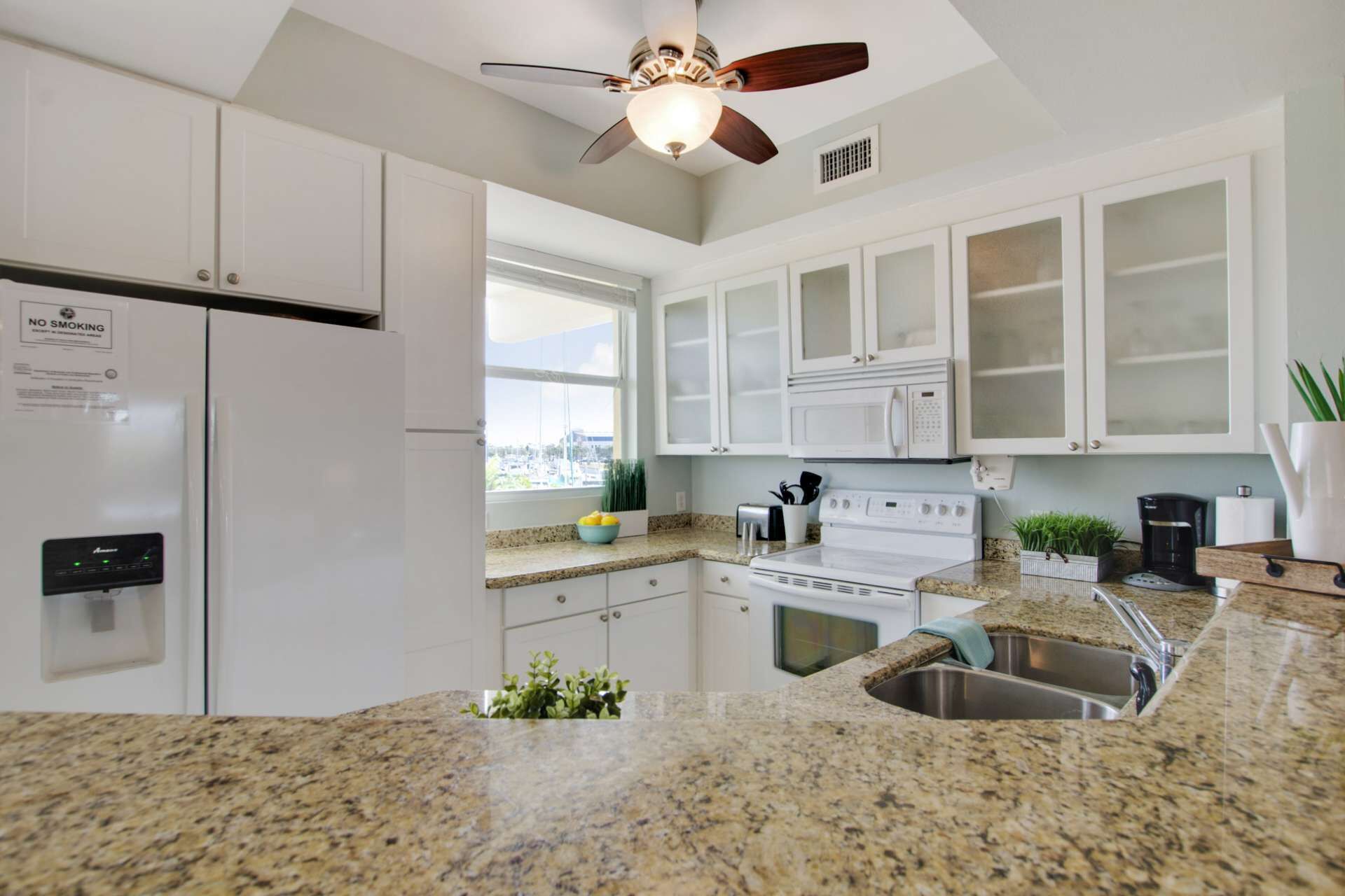 A modern kitchen with white cabinets, granite countertops, a built-in oven, and a stainless steel sink.
