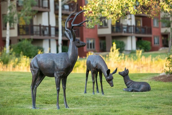 Une sculpture de cerf se trouve dans une zone herbeuse, avec un bâtiment en arrière-plan.