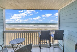 A balcony with a view of the beach, featuring a table and two chairs.
