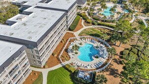 A hotel with multiple floors, a rooftop pool, and a landscaped pool area with lounge chairs.