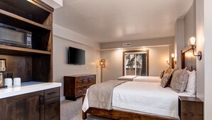 A bedroom with a wooden bed frame, a TV mounted on the wall, and a window with a view of trees. - Walk to Main Street/Town Lift I Hot Tub I Sauna I Managed by Park City Lodging (PARK CITY)