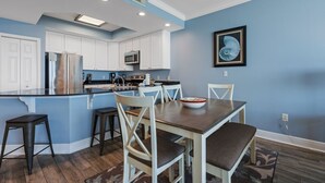 A kitchen with white cabinets, a central island, and a dining table with chairs. - Beachfront w/ Expansive Gulf Front View | Pool, Outdoor Grills, Sauna | Sleeps 7 (Gulf Shores)