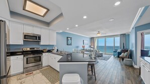 A modern kitchen with stainless steel appliances, a central island, and a dining area with a view. - Beachfront w/ Expansive Gulf Front View | Pool, Outdoor Grills, Sauna | Sleeps 7 (Gulf Shores)