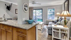 A modern kitchen with granite countertops, wooden cabinets, and a blue bowl. There is a dining area with a white table and a lamp. - Beautiful Beachside Villa! Oceanfront Pool (Hilton Head)