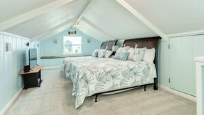 Un dormitorio con techo inclinado, una cama con ropa de cama floral, un escritorio y una ventana con vistas.