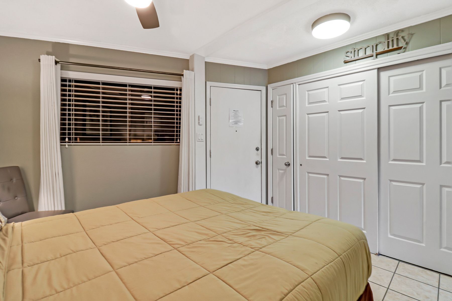 Une chambre à coucher avec un lit, une fenêtre avec des stores, une armoire et un luminaire au plafond.