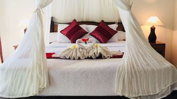 Una cama con dosel, dos almohadas rojas y una presentación de toallas.