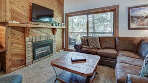 A cozy living room with a fireplace, wooden walls, a large window, and a leather couch.
