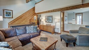 A spacious living area with a high ceiling, wooden beams, a sofa, a coffee table, and a dining table.