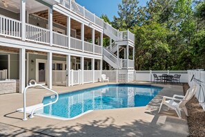A two-story building with a swimming pool, outdoor furniture, and a white fence.