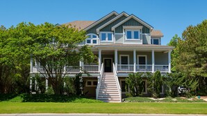 Ein zweigeschossiges Haus mit Veranda, einer Treppe zum Eingang und einem gepflegten Rasen.