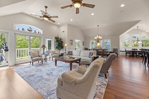 A spacious living room with a high ceiling, large windows, and a dining area with wooden furniture. - Witches Bikini: Private Pool, Hot Tub, Club Access (Corolla)