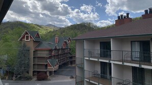 A multi-story building with balconies, a parking area, and a view of a mountainous landscape.