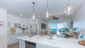 A modern kitchen with a large island, pendant lights, and a view of the ocean. - Beachfront, Poolside, Kayaks for snorkeling the reef! (West End)