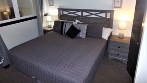 A neatly made bed with a quilted cover, two bedside tables with lamps, and a window with curtains. - Snowflake Lodge conveniently located ski in/out sleep 6 Close to Restaurants (Copper)