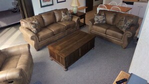 A living room with a brown sofa set, a wooden coffee table, and a dining area with a white table and chairs. - Snowflake Lodge conveniently located ski in/out sleep 6 Close to Restaurants (Copper)