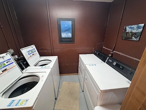 A laundry room with two washing machines and dryers, a small rug, and a framed picture on the wall.