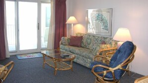 Una sala de estar con un sofá, dos sillones, una mesa de centro de vidrio y un cuadro en la pared.