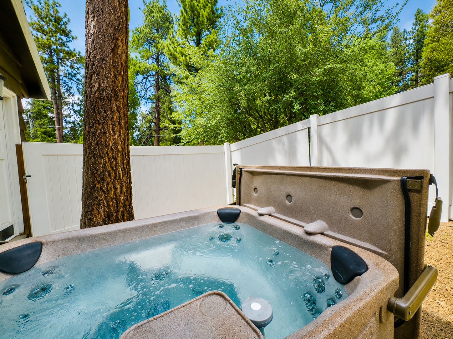 An outdoor hot tub with a stone exterior, surrounded by a white fence and trees.