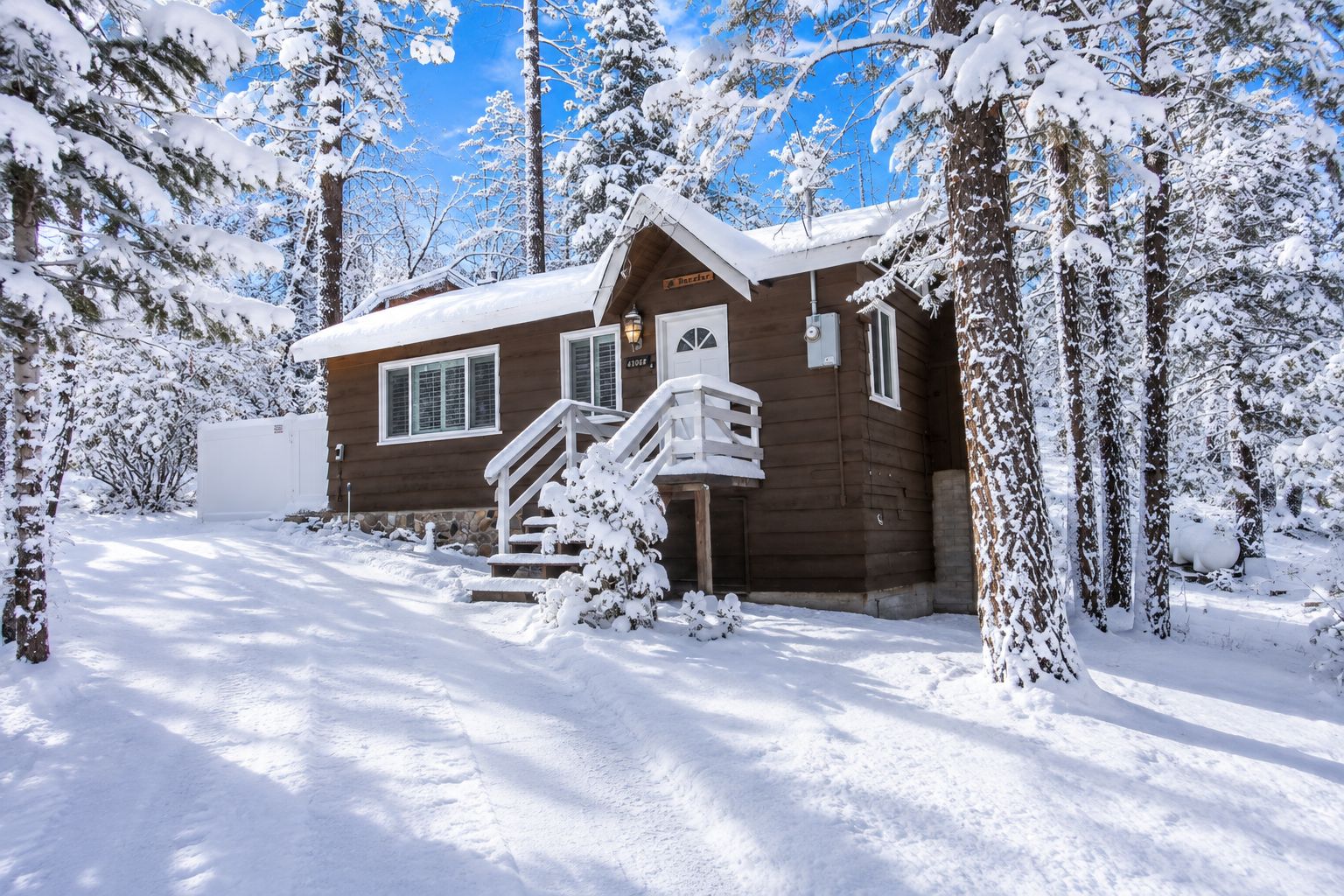 Una cabaña de madera con un porche y escalones, rodeada de árboles cubiertos de nieve.