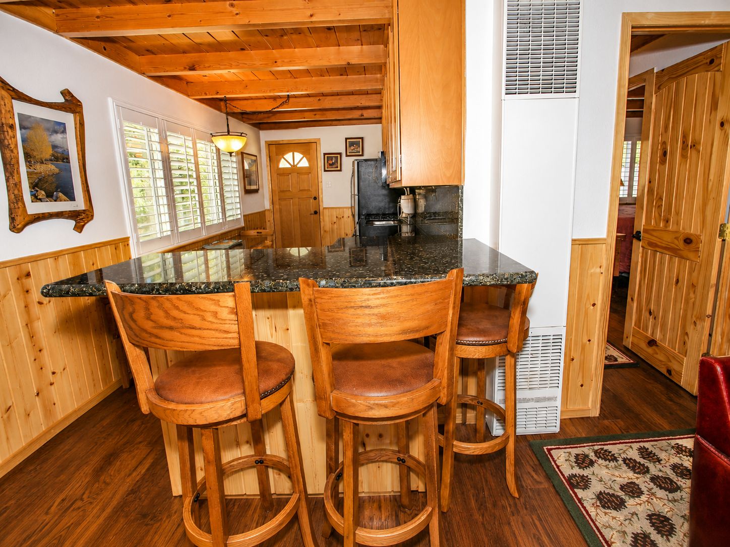 Una cocina con encimera de granito, sillas de madera y techo de madera.