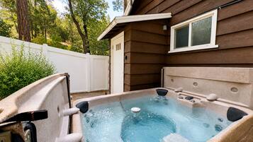 A hot tub with a pump and jets, surrounded by a wooden deck and a white fence.
