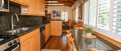 A kitchen with wooden cabinets, a granite countertop, a built-in oven, and a dining area with wooden chairs.