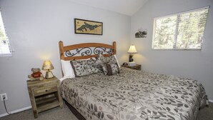 Quarto com cabeceira de madeira, colcha florida, mesa de cabeceira com abajur, um ursinho de pelúcia e um mapa na parede.
