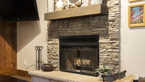 A stone fireplace with a TV above it, a stone wall, and a painting on the wall. - Managed by Park City Lodging-Walk to Main Street/Town Lift-Common Hot Tub/Sauna (PARK CITY)