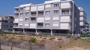 En flervåningsbyggnad med bostäder, balkonger och en sandig marknivå.