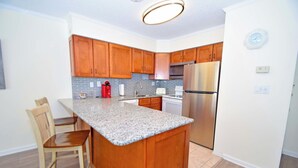 A modern kitchen with wooden cabinets, a granite countertop, stainless steel appliances, and a built-in island with bar stools.
