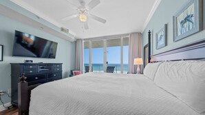 Habitación de hotel con una cama grande, televisión, ventilador de techo y balcón con vista al océano.