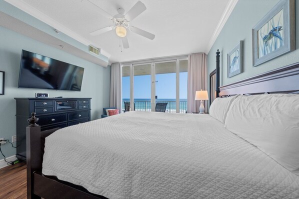 Habitación de hotel con una cama grande, televisión, ventilador de techo y balcón con vista al océano.